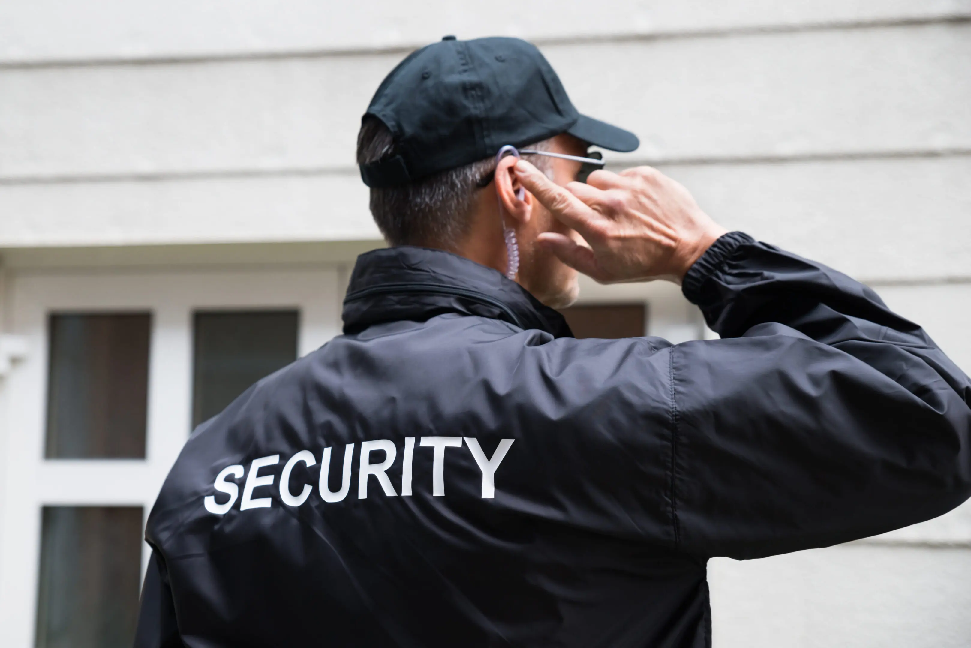 Rear view of mature security guard listening to earpiece against building